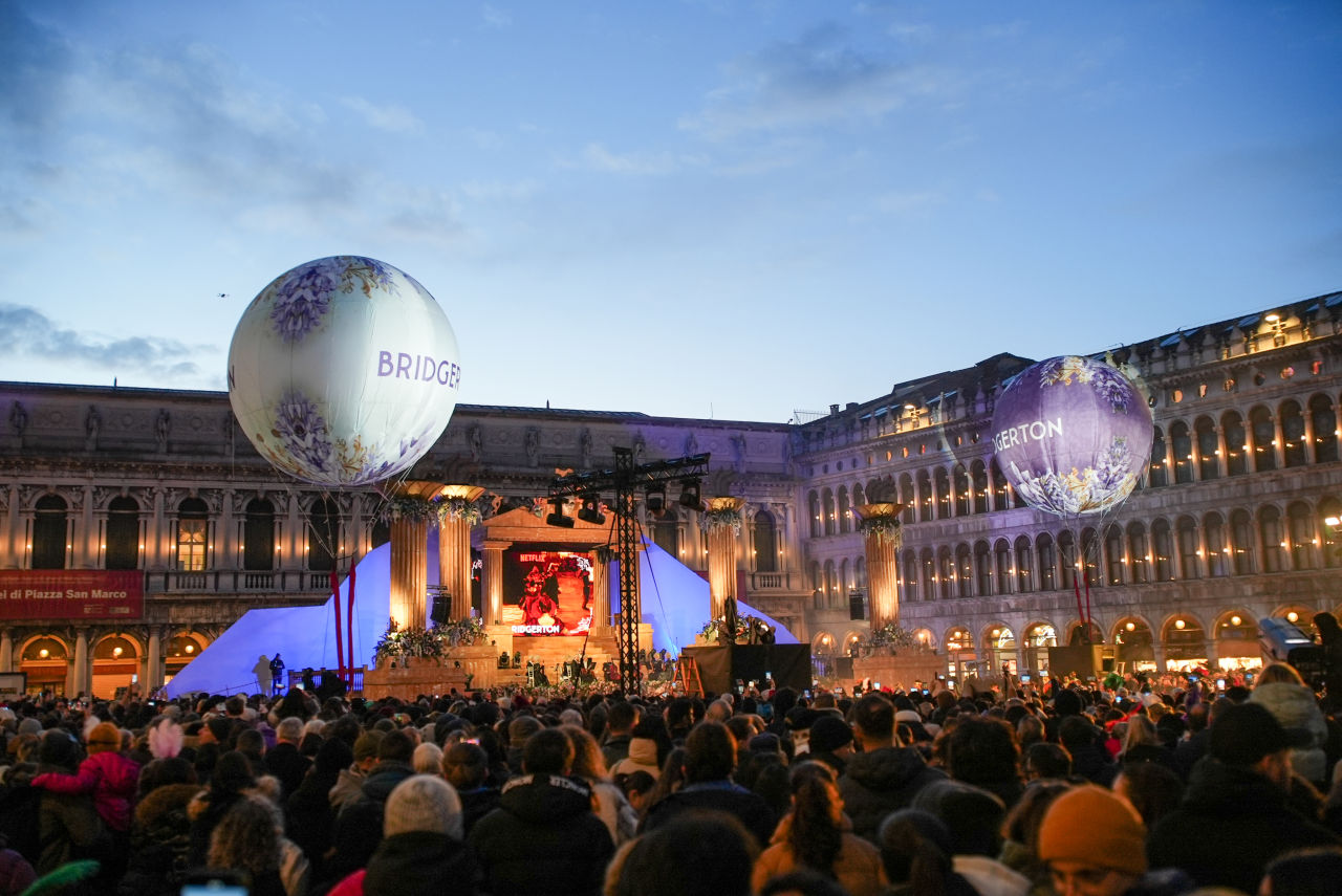 Crowds gather in St. Mark’s Square in Venice during Carnival as Bridgerton-branded hot air balloons float above a nighttime celebration